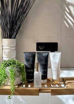 Haircare product display featuring Hydrating Shampoo for Hair Extensions in a white tube with gold accents beside black and white bottles.