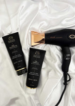 Nourishing Conditioner for Hair Extensions in a black tube with gold lettering and a clear cap, beside shampoo and a hair dryer.